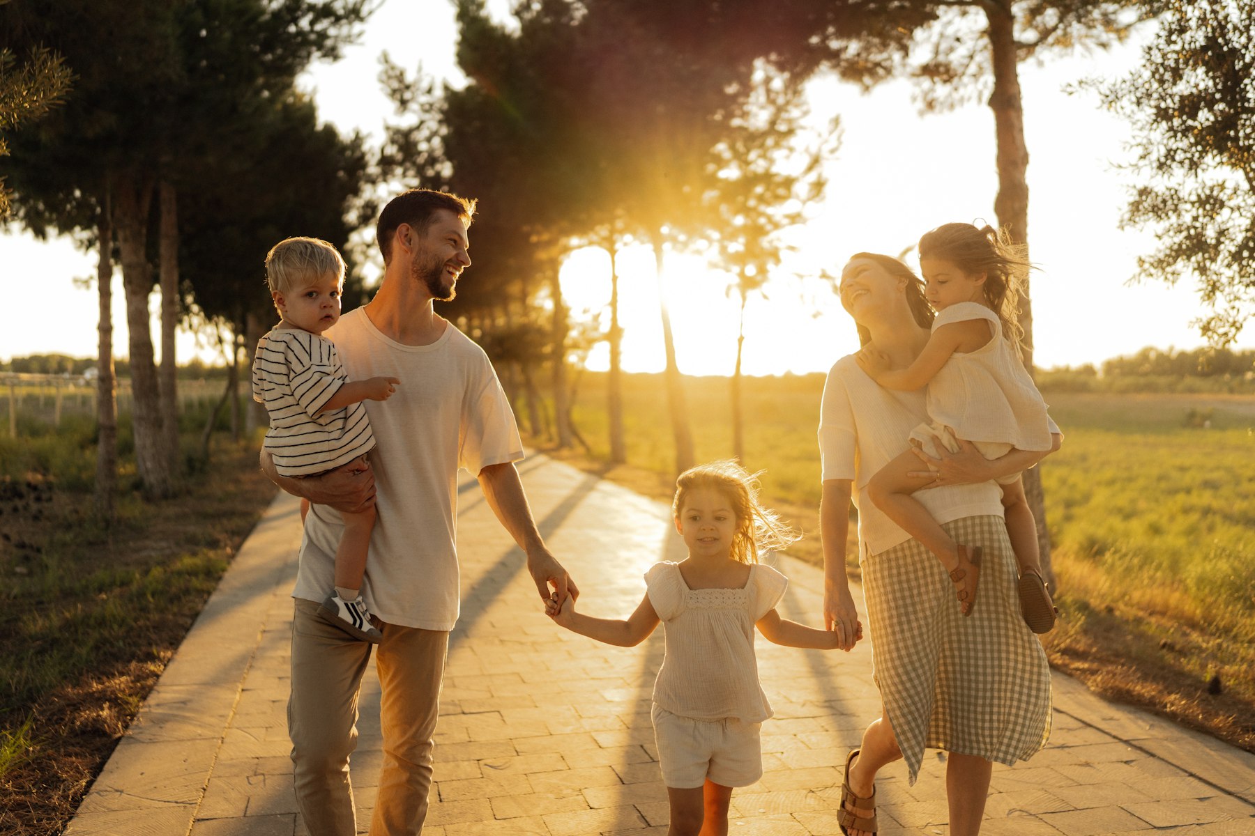 A family walking together along a sunlit path at golden hour, parents and children close and laughing.